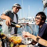 Ein Mann schenkt einem anderen reichen Mann Champagner ein, er sitzt auf einer Yacht