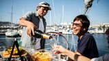 Ein Mann schenkt einem anderen reichen Mann Champagner ein, er sitzt auf einer Yacht