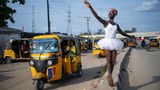 Eine Ballettschülerin in weißem Tutu posiert am Straßenrand vor einem gelben Tuktuk.