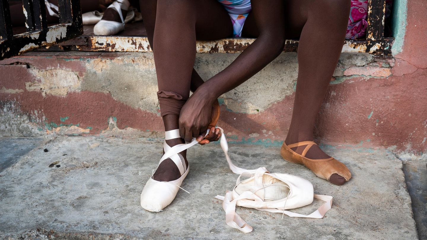 Eine Ballettschülerin bindet einen Spitzenschuh an ihrem rechten Fuß Eine Ballettschülerin bindet einen Spitzenschuh an ihrem rechten Fuß