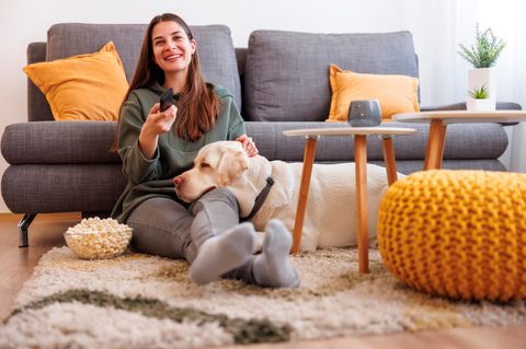 Mit TV-Stick schaut eine Frau mit ihrem Hund fernsehen.