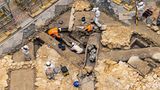 Eine Aufnahme von oben zeigt, wie Archäologen den Boden absuchen und einen Sarkophag bergen