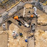 Eine Aufnahme von oben zeigt, wie Archäologen den Boden absuchen und einen Sarkophag bergen