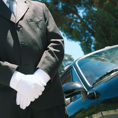 Vor einem Oldtimer steht ein Butler in Livree und weißen Handschuhen