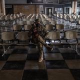 Ein vermummter Mann sitzt in einer Wartehalle auf einem von vielen Stühlen.