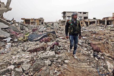 Ein Kämpfer läuft mit einem Gewehr durch Ruinen im syrischen Kobane.