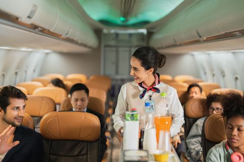 Eine Stewardess bietet auf einer Flug-Reise einem Passagier Getränke an