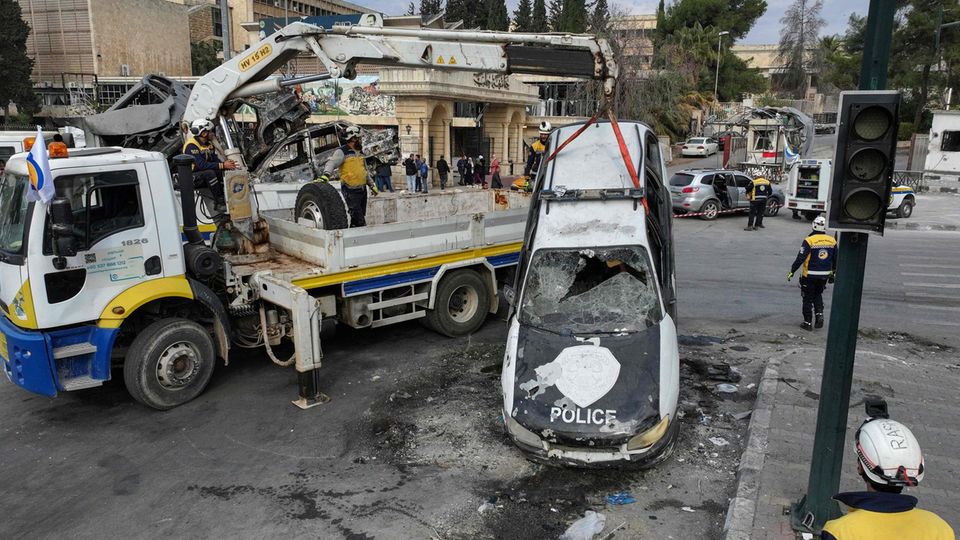 Mitglieder der Weißhelme entfernen ein ausgebranntes Polizeiauto von der Straße Mitglieder der Weißhelme entfernen ein ausgebranntes Polizeiauto von der Straße