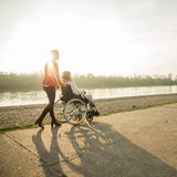 Eine Frau schiebt eine Frau im Rollstohl am Ufer eines Flusses entlang