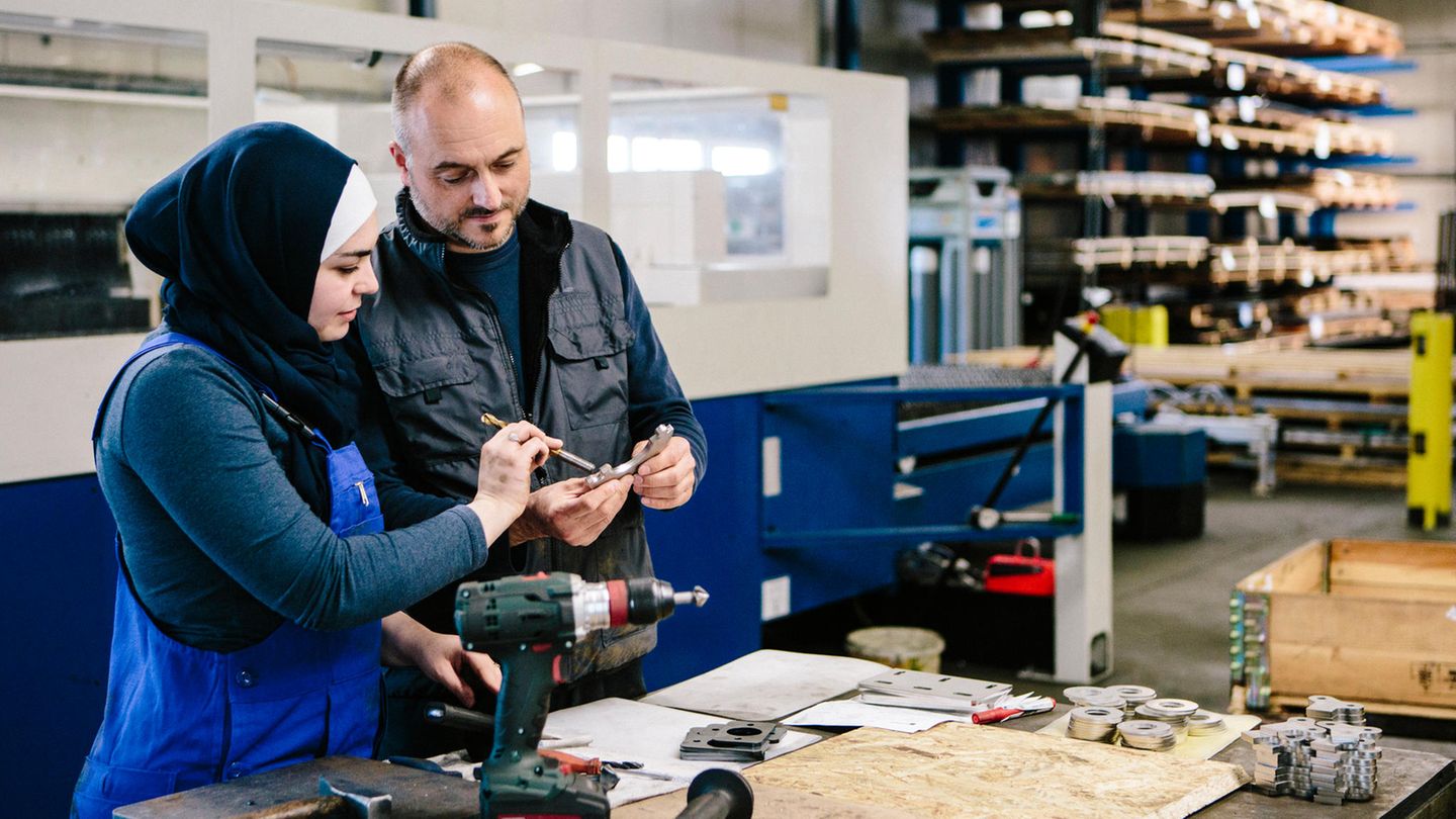 Ein Meister erklärt einer Auszubildenden ein Arbeitsgerät