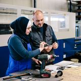 Ein Meister erklärt einer Auszubildenden ein Arbeitsgerät