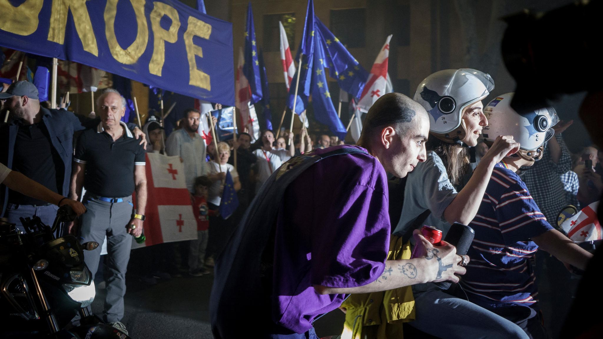 Georgien: Ein Mann spielt während der Proteste Musik mit seiner Box. Im Hintergrund der Protest und ein "Europa"-Banner