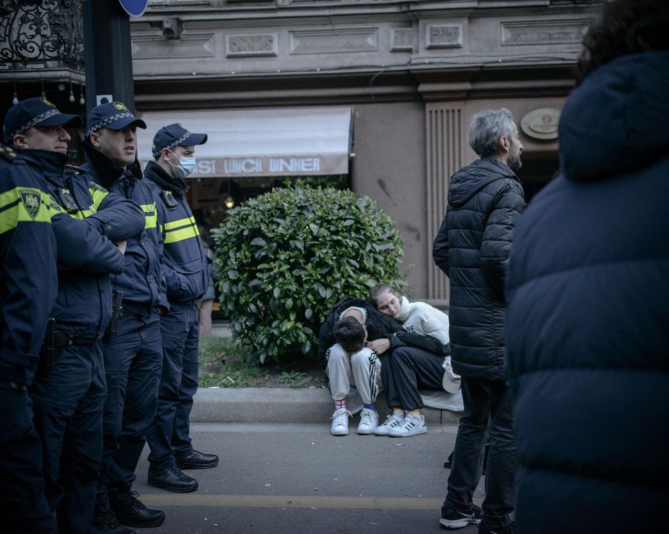 Zwei Personen sitzen auf der Bordsteinkante. Die Polizei steht daneben