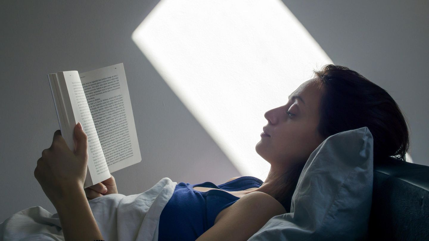 Eine Frau liegt im Bett und liest ein Buch.