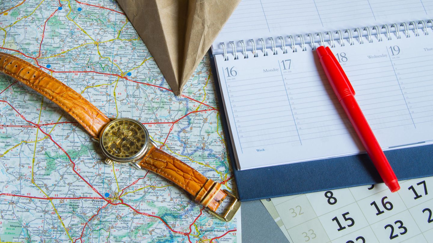 Brückentage: Eine Armbanduhr, ein Kalender und ein Papierflieger auf einer Landkarte