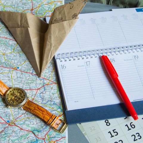 Brückentage: Eine Armbanduhr, ein Kalender und ein Papierflieger auf einer Landkarte