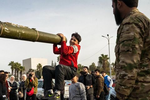 Ein Jugendlicher hält sich in Damaskus aus lauter Freude über den Umsturz in Syrien an einem Panzerrohr fest