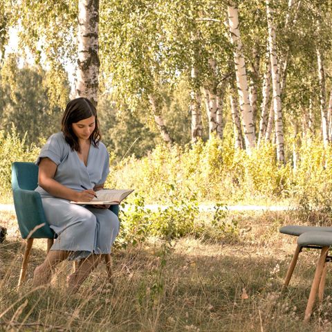 Polyamorie: Frau sitzt vor leeren Stühlen im Wald