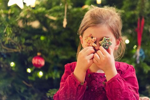 Ein Mädchen hält sich Kekse vor die Augen und steht vor einem Weihnachtsbaum