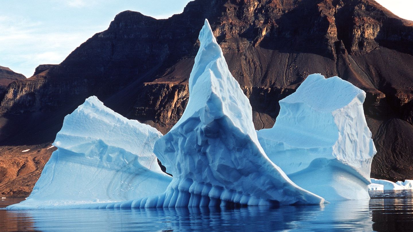 Ein Eisberg dümpelt an einer grau-braunen Landschaft vorbei