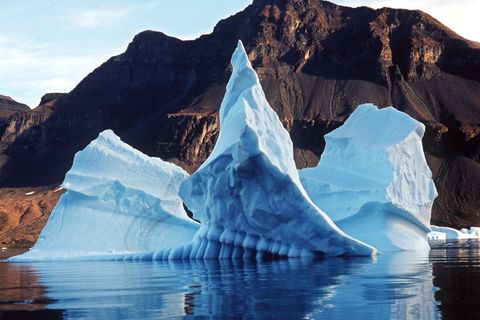 Ein Eisberg dümpelt an einer grau-braunen Landschaft vorbei
