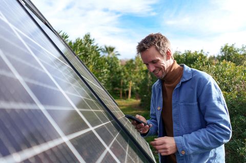 Ein Mann trackt auf seinem Handy die Daten der PV-Anlage mithilfe des Wechselrichters.