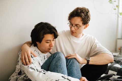 Bebilderung Psychische Erkrankung: Zwei Männer sitzen nebeneinander, der eine hat den anderen in den Arm genommen
