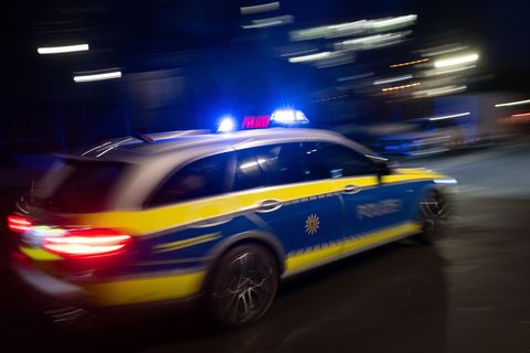 Ein Polizeifahrzeug fährt mit Blaulicht an einem Gebäude vorbei