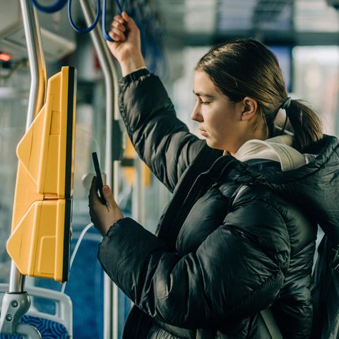 A young woman rides on a tram and uses the ticket machine with her cell phone.