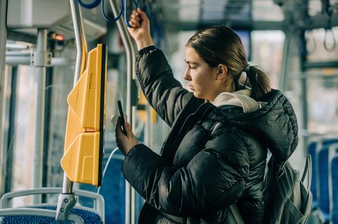 Eine junge Frau fährt in einer Straßenbahn und bedient den Ticketautomaten mit dem Handy.
