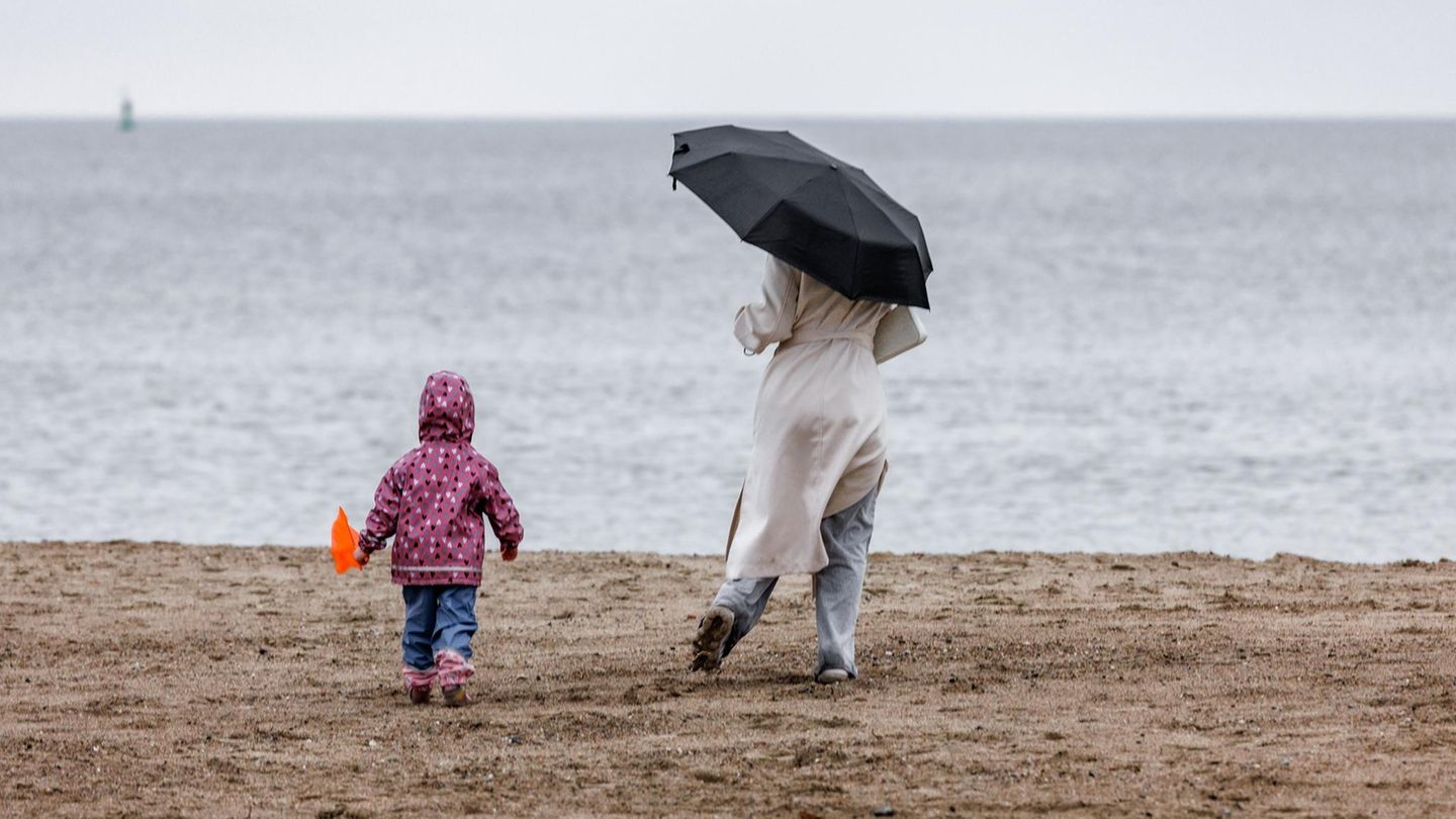 Eine Frau mit Schirm und ein Kind sind bei diesig trübem Wetter am Ostsee-Strand in Travemünde unterwegs