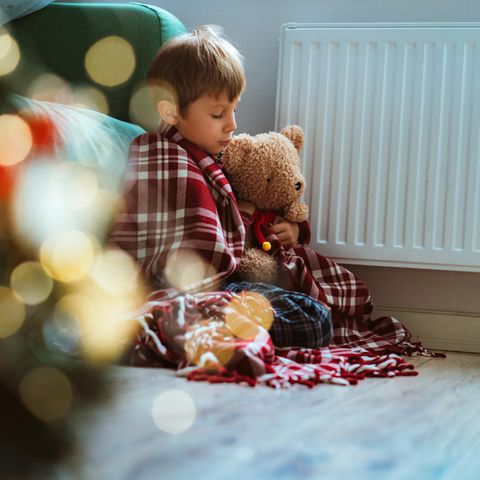 Kinderarmut Kindergrundsicherung: Junge sitzt mit Teddy eingekuschelt vor der Heizung