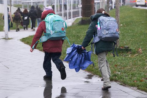 Regen-Wetter: Zwei Kinder mit Schirmen laufen über eine Straße