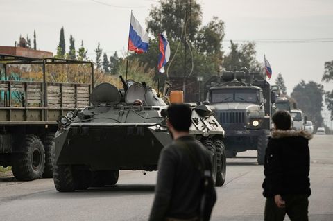 Kämpfer aus Syrien beobachten die Vorbeifahrt russischer Panzerfahrzeuge in der Nähe des syrischen Luftwaffenstützpunkts Hmeimim