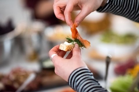 Frau legt eine Scheibe Räucherlachs auf ein Stück Baguette