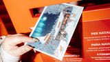 Eine Postkarte mit einer Illustration des Weihnachtsmanndorfes wird in Briefkasten geworfen