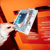Eine Postkarte mit einer Illustration des Weihnachtsmanndorfes wird in Briefkasten geworfen