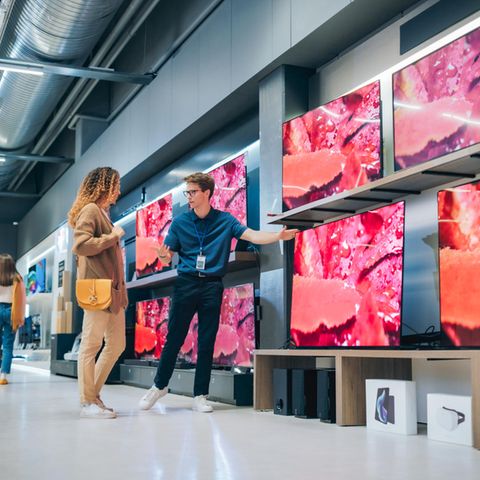 Stiftung Warentest Fernseher: Ein Verkäufer zeigt einer Frau verschiedene TV-Modelle