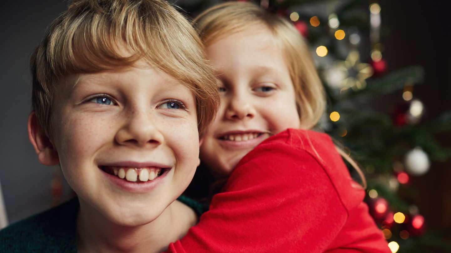 Familie: Kinder umarmen sich vor dem Weihnachtsbaum