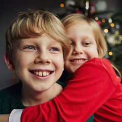 Familie: Kinder umarmen sich vor dem Weihnachtsbaum