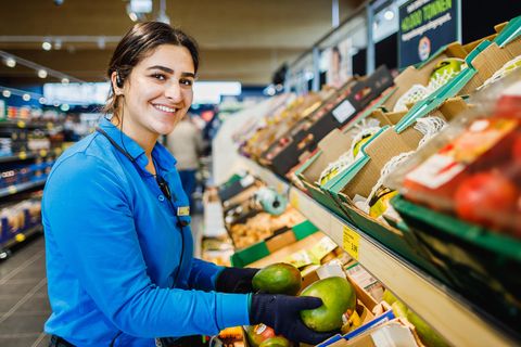 Verkäuferin bei Aldi sortiert Mangos in der Gemüseabteilung