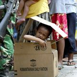 Einen Monat nach dem Tsunami schaut ein Junge am 26. Januar 2005 in einem Notlager auf Sumatra in der Schlange der Essensausgabe aus einem Pappkarton