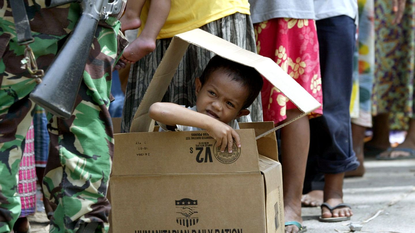 Einen Monat nach dem Tsunami schaut ein Junge am 26. Januar 2005 in einem Notlager auf Sumatra in der Schlange der Essensausgabe aus einem Pappkarton