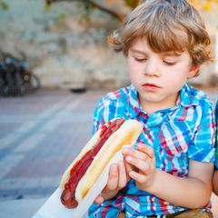 Familienessen: Ein Junge schaut skeptisch auf seinen Hotdog