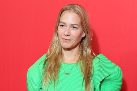 Franka Potente posiert in einem grünen Kleid vor einer roten Wand