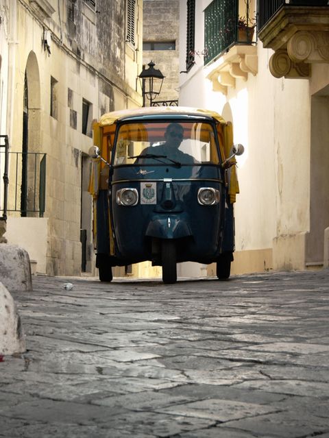 Eine Piaggio Ape fährt durch enge Gassen einer italienischen Stadt