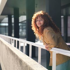 Symbolbild Neujahrsvorsätze: Eine Frau steht an einem Balkon und wirkt zufrieden