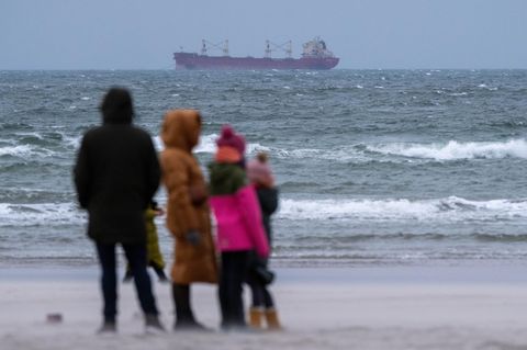 Zwei Erwachsene und zwei Kinder schauen bei viel Wind am Strand von Warnemünde auf die Ostsee