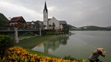 Ein Arbeiter sprüht Wasser auf die Blumen, die den Nachbau des österreichischen Ortes Hallstatt umranden. Das Stahlunternehmen Minmetals ließ die Wohnsiedlung vor mehr als zehn Jahren für knapp eine Milliarde Euro in der Stadt Luoyangzhen in Südchina errichten. Zur Eröffnung reiste auch der Bürgermeister des echten Hallstatt an, ein Ort im Salzkammergut, den die UNESCO zum Weltkulturerbe ernannt hat. Statt einer Alpenkulisse ragen auf der anderen Seite des Sees Hochhäuser in den Himmel