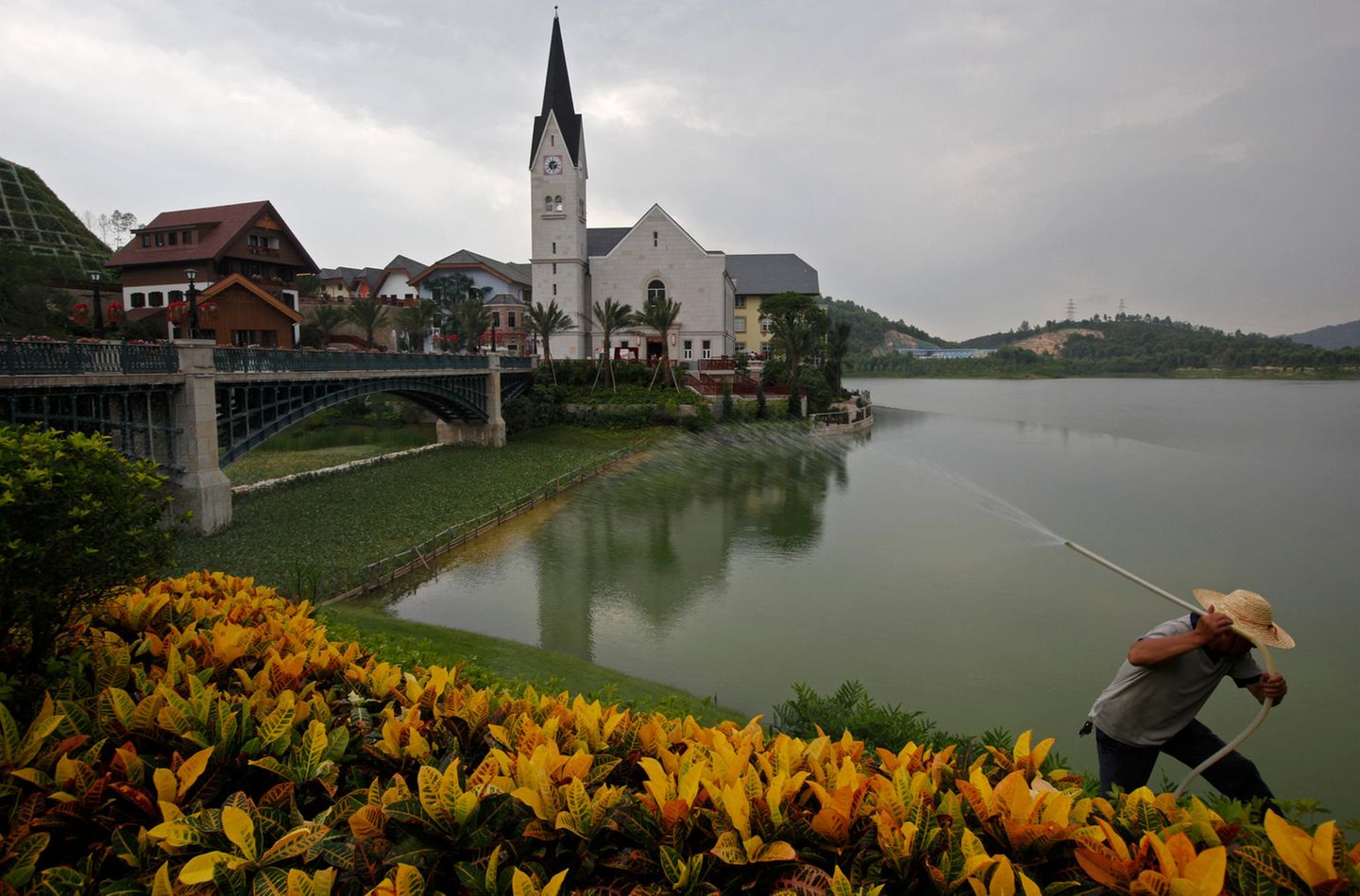 Ein Arbeiter sprüht Wasser auf die Blumen, die den Nachbau des österreichischen Ortes Hallstatt umranden. Das Stahlunternehmen Minmetals ließ die Wohnsiedlung vor mehr als zehn Jahren für knapp eine Milliarde Euro in der Stadt Luoyangzhen in Südchina errichten. Zur Eröffnung reiste auch der Bürgermeister des echten Hallstatt an, ein Ort im Salzkammergut, den die UNESCO zum Weltkulturerbe ernannt hat. Statt einer Alpenkulisse ragen auf der anderen Seite des Sees Hochhäuser in den Himmel